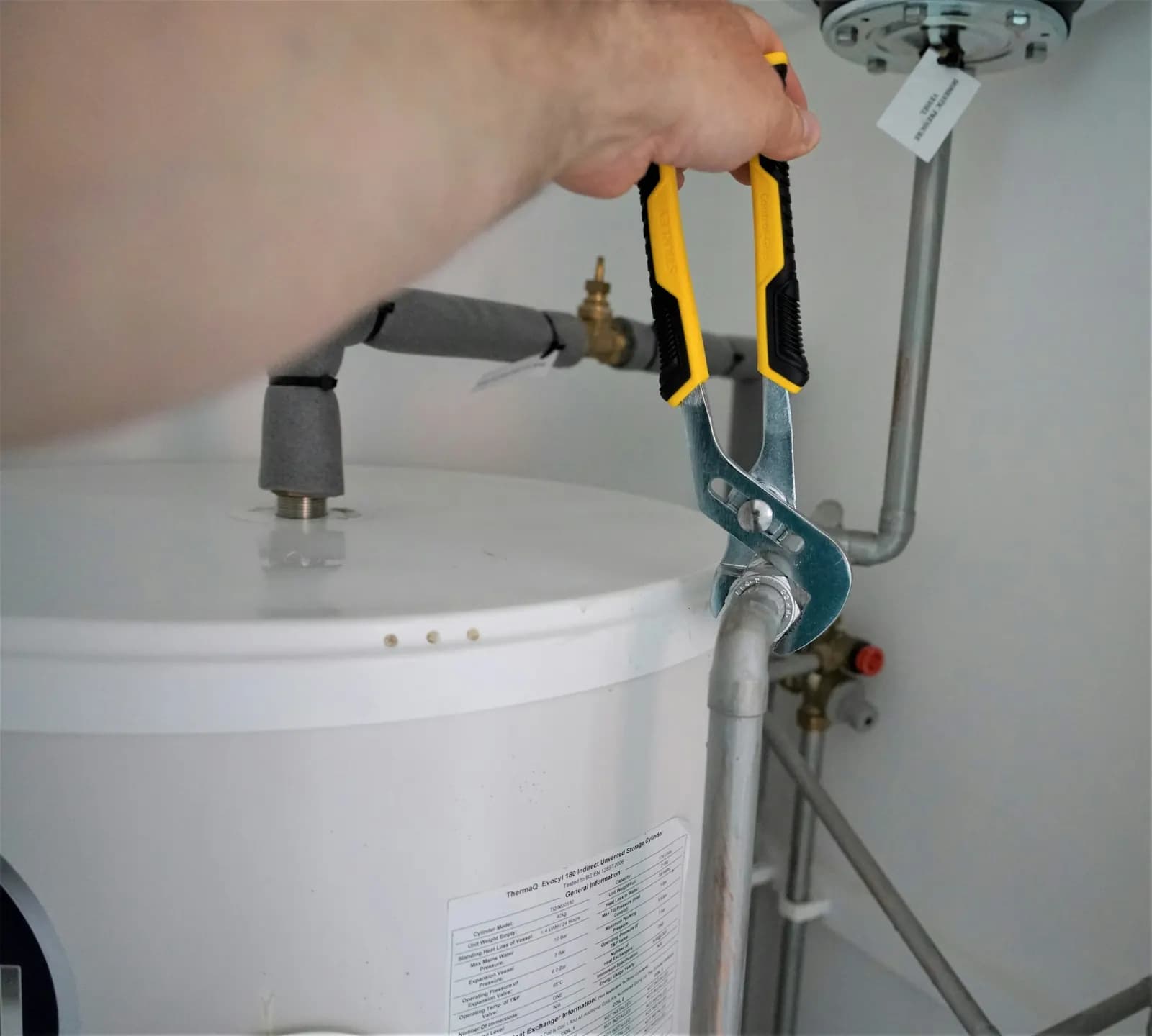 Mains d’un installateur raccordant un chauffe-eau au réseau d’eau, pince en main