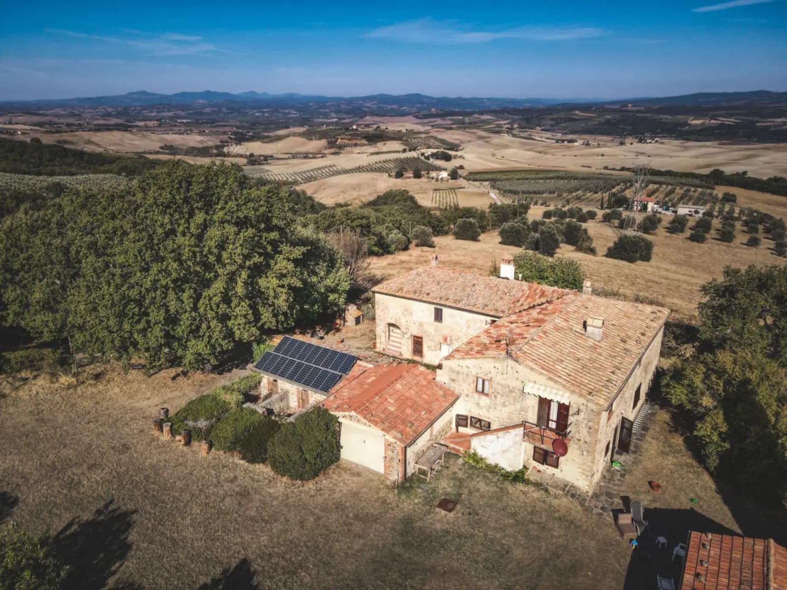 Mas en pierre entouré de collines, quelques panneaux solaires sur un toit, vu du ciel