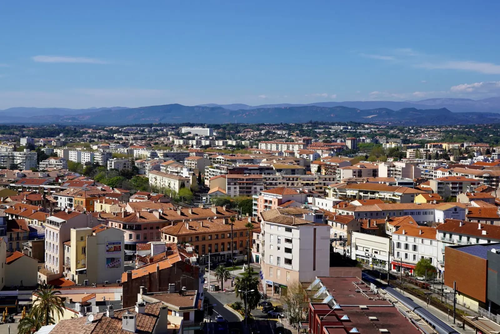 Toits de tuiles et immeubles d’une ville, montagnes à l’horizon