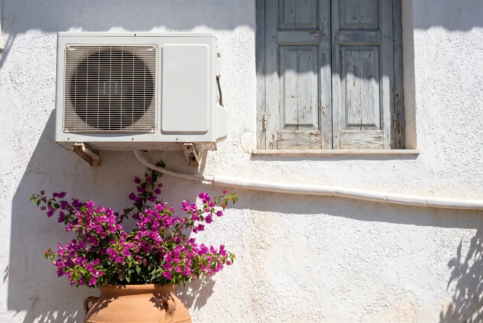 Unité extérieure de climatisation fixée sur une façade blanche, sous une fenêtre
